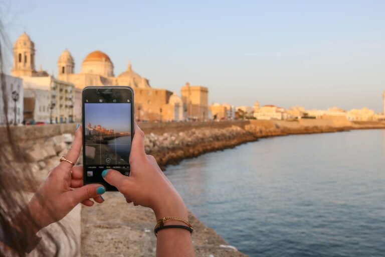 Woman photographing beautiful Cadiz waterfront scene with smartphone during golden hour.